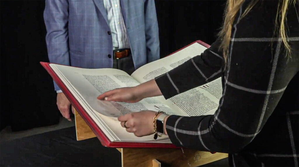 A guest carefully turns a page from the corner and supports it with their other hand. Notice their jewelry and remain cautious so it doesn’t scrape or come in contact with the pages of your Heritage Edition (9:00). 